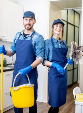 Portrait of a couple as a professional cleaners in uniform standing together with cleaning tools indoors